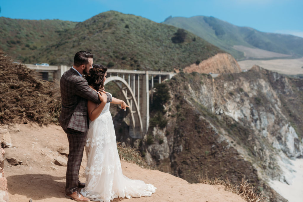 Couple looking out to the water on cliffs of Big Sur with wedding dress and suit on.