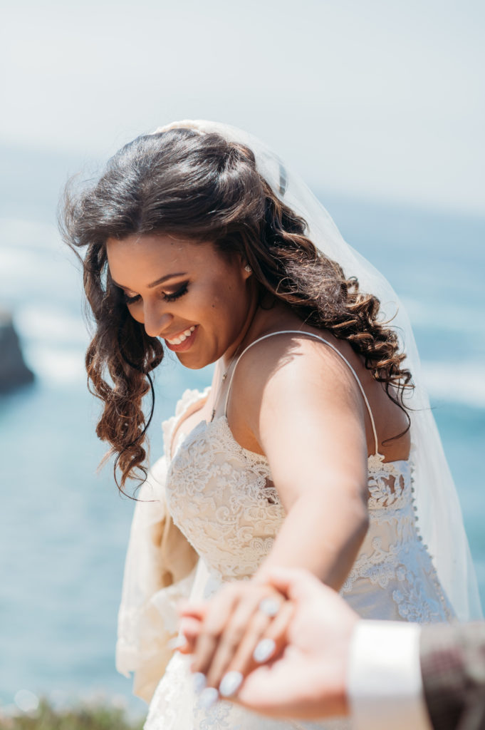 Bride details with her looking down and holding groom's hand on the cliffs of Big Sur.